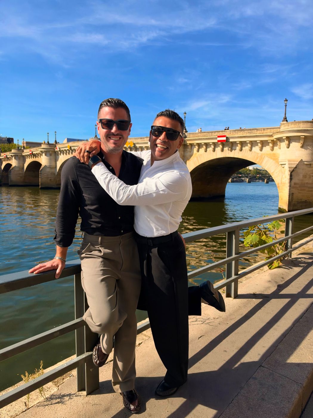 Elie and Justin laughing by the Seine with the Pont Neuf behind them